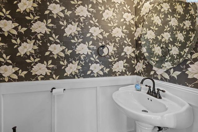 bathroom with wallpapered walls, a wainscoted wall, a sink, and a decorative wall