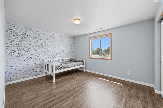 bedroom featuring wallpapered walls, an accent wall, baseboards, and wood finished floors