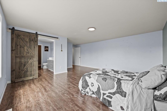 bedroom with a barn door, wood finished floors, baseboards, and connected bathroom