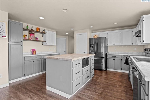 kitchen with appliances with stainless steel finishes, wall chimney range hood, a center island, dark wood-style flooring, and light countertops