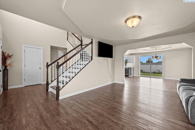 unfurnished living room with wood finished floors, baseboards, arched walkways, and stairs