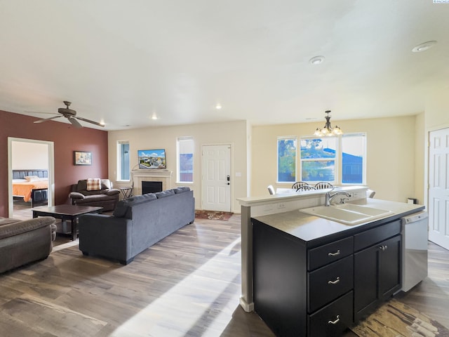 kitchen featuring dishwasher, dark cabinets, light wood-style floors, a fireplace, and a sink