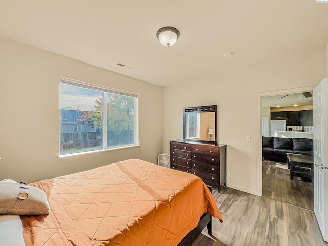 bedroom with visible vents, wood finished floors, freestanding refrigerator, and baseboards