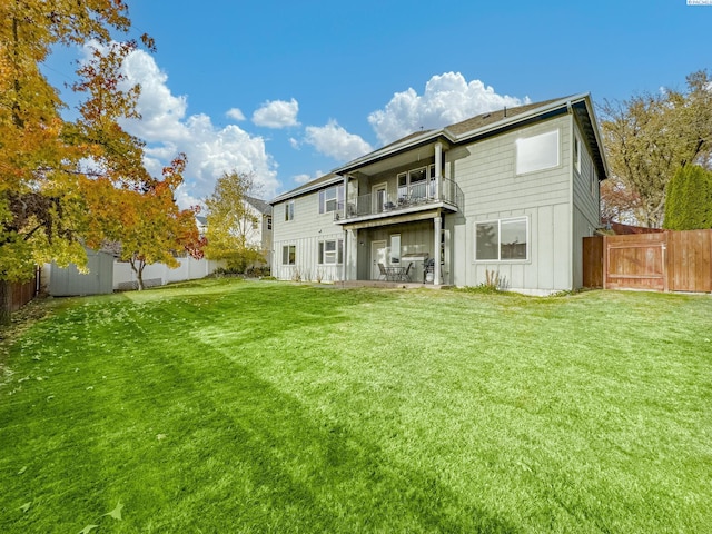 back of property featuring board and batten siding, a fenced backyard, a yard, and a balcony