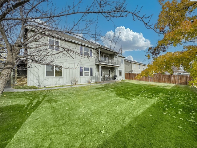 rear view of property with a balcony, board and batten siding, fence, and a lawn