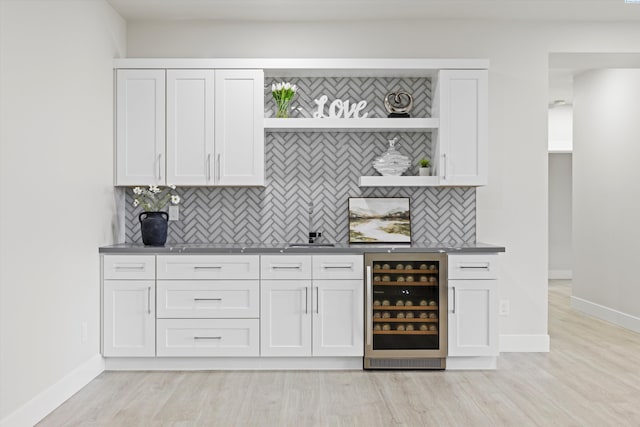 bar featuring wine cooler, white cabinetry, tasteful backsplash, and light hardwood / wood-style flooring