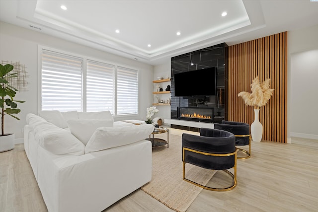 living room featuring a large fireplace, a raised ceiling, and light hardwood / wood-style floors