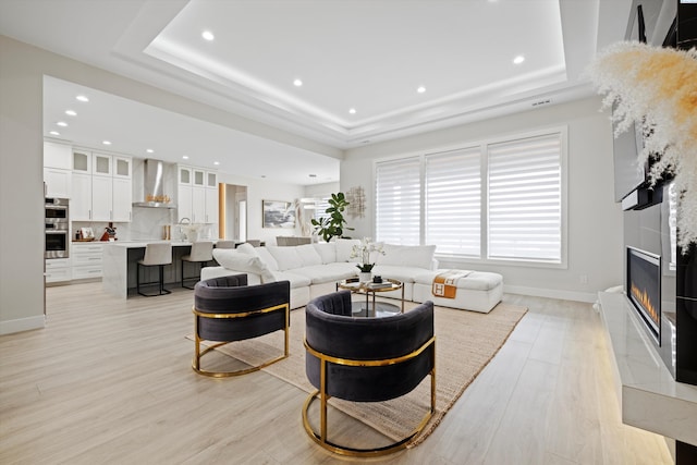 living room featuring light hardwood / wood-style flooring, a tray ceiling, and a fireplace