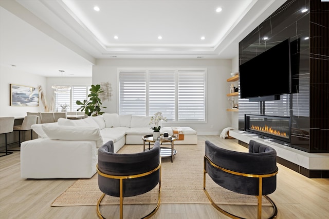 living room with light hardwood / wood-style flooring, a fireplace, and a raised ceiling