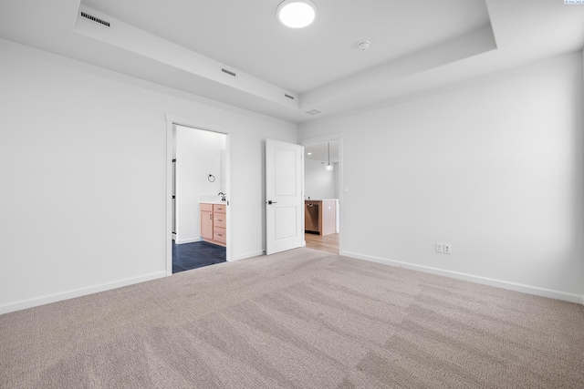 unfurnished bedroom featuring ensuite bathroom, carpet flooring, and a raised ceiling