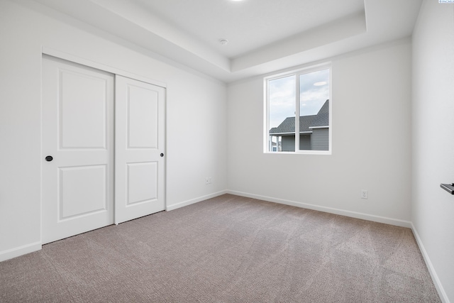 unfurnished bedroom featuring a raised ceiling, carpet flooring, and a closet