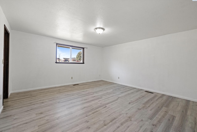 spare room with light wood-style floors, baseboards, and visible vents