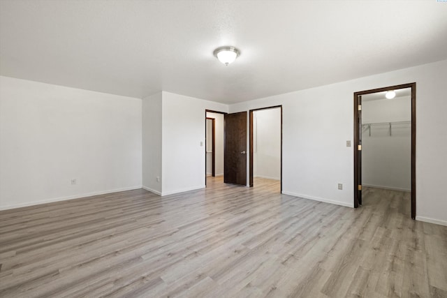 unfurnished bedroom featuring light wood finished floors, baseboards, a walk in closet, and a closet