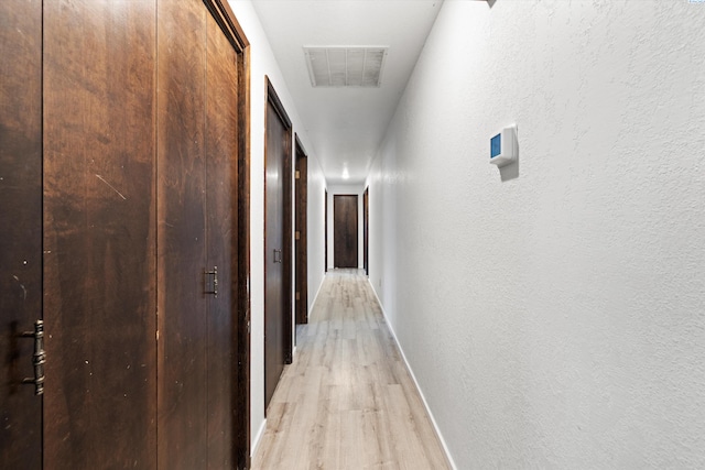 corridor featuring a textured wall, light wood-style flooring, visible vents, and baseboards