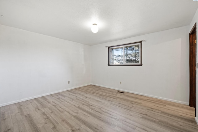 spare room featuring baseboards, visible vents, a textured ceiling, and light wood finished floors