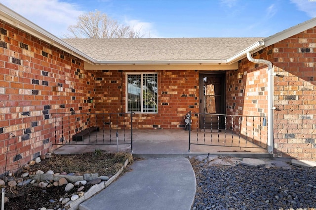 entrance to property with a shingled roof and brick siding