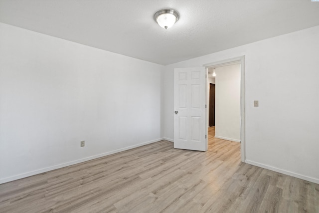 spare room featuring baseboards, a textured ceiling, and light wood-style floors