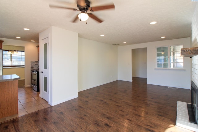 unfurnished living room featuring hardwood / wood-style flooring, a brick fireplace, plenty of natural light, and ceiling fan with notable chandelier