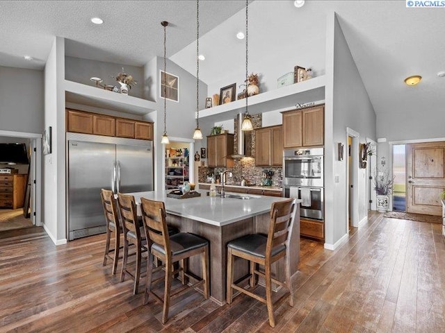 kitchen with brown cabinets, high vaulted ceiling, appliances with stainless steel finishes, and a breakfast bar area
