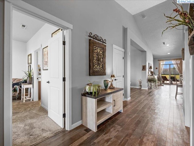 hall featuring dark wood-style flooring, baseboards, visible vents, and lofted ceiling