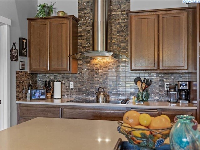 kitchen with backsplash, black electric cooktop, brown cabinets, and wall chimney exhaust hood