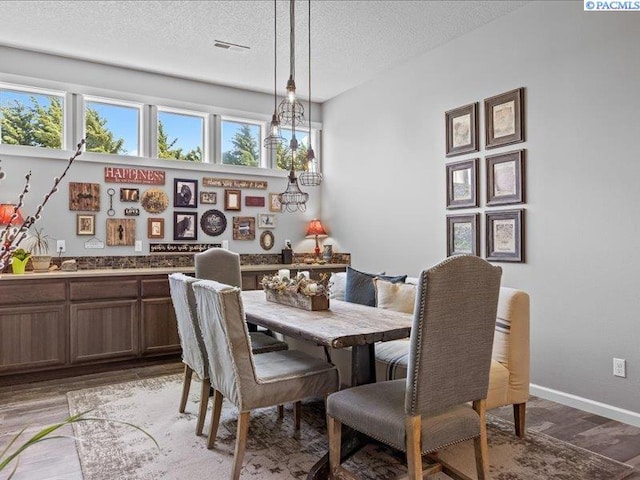 dining room with baseboards, light wood finished floors, a textured ceiling, and visible vents