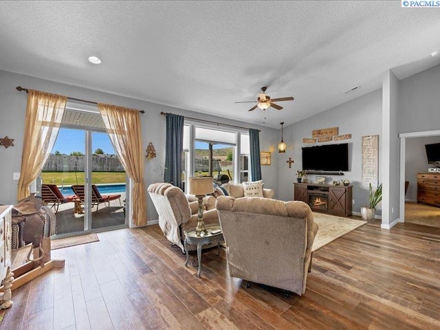 living area with a textured ceiling, ceiling fan, vaulted ceiling, and wood finished floors
