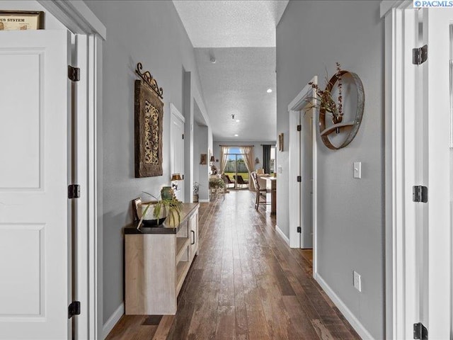 corridor with dark wood-type flooring, a textured ceiling, and baseboards
