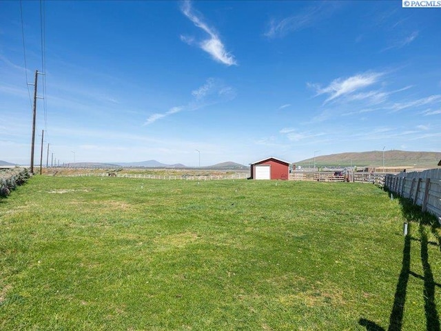 view of yard with an outdoor structure, a rural view, fence, and a mountain view