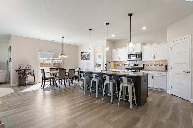 kitchen featuring stainless steel appliances, a kitchen island with sink, white cabinets, and light stone counters