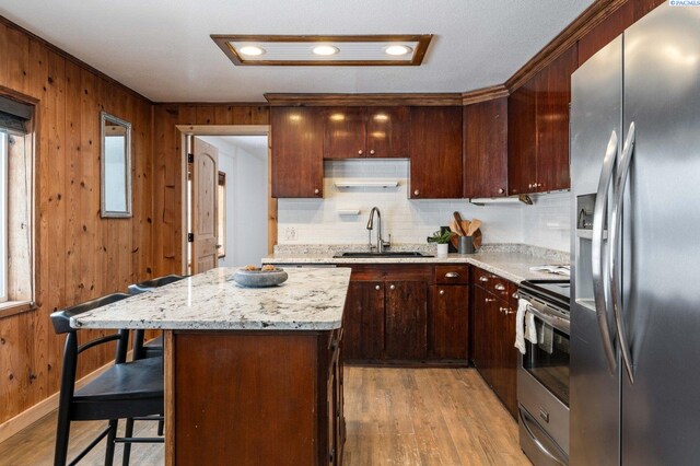 kitchen featuring sink, a breakfast bar area, appliances with stainless steel finishes, a center island, and light stone counters