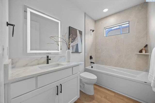 full bathroom featuring tiled shower / bath combo, vanity, hardwood / wood-style flooring, and toilet