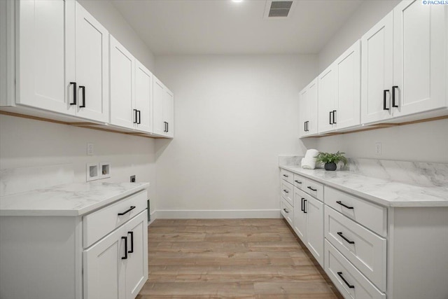 washroom with electric dryer hookup, washer hookup, light hardwood / wood-style floors, and cabinets