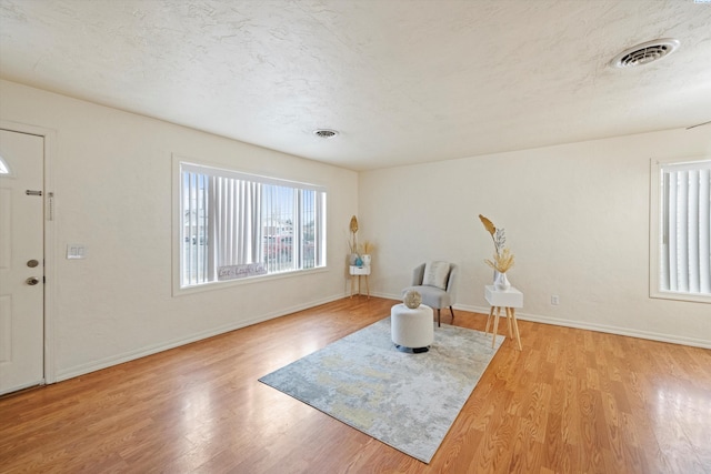 sitting room with a textured ceiling, light wood finished floors, visible vents, and baseboards