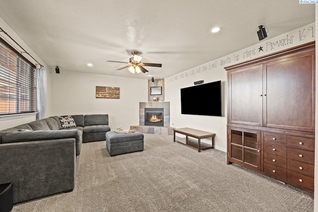 living room with ceiling fan, light colored carpet, a fireplace, and a textured ceiling