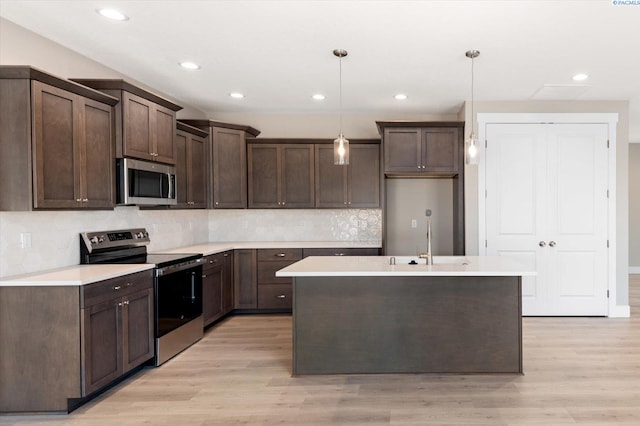 kitchen with appliances with stainless steel finishes, sink, pendant lighting, and light hardwood / wood-style floors