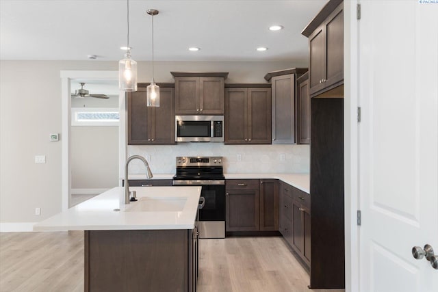 kitchen with appliances with stainless steel finishes, decorative light fixtures, an island with sink, sink, and decorative backsplash