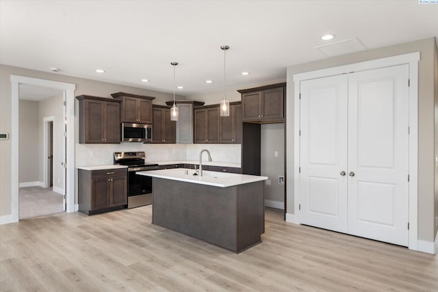 kitchen featuring appliances with stainless steel finishes, decorative light fixtures, a kitchen island with sink, dark brown cabinets, and light wood-type flooring