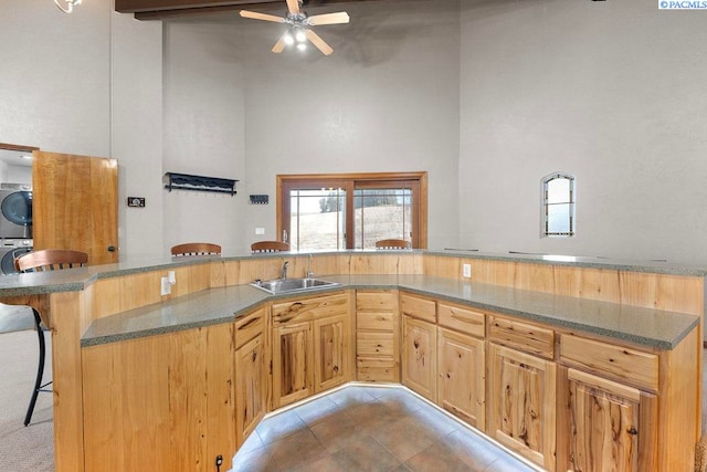 kitchen featuring dark stone counters, stacked washer / dryer, a kitchen breakfast bar, a high ceiling, and a sink