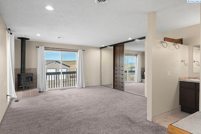 unfurnished living room featuring a healthy amount of sunlight, light colored carpet, a textured ceiling, and a wood stove