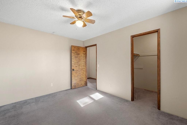 unfurnished bedroom with a textured ceiling, a spacious closet, ceiling fan, and carpet flooring