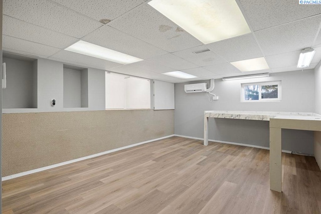 basement featuring a drop ceiling, wood finished floors, and a wall mounted AC