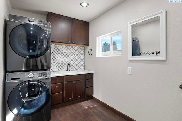 laundry area with stacked washer and dryer, a sink, baseboards, cabinet space, and dark wood-style floors