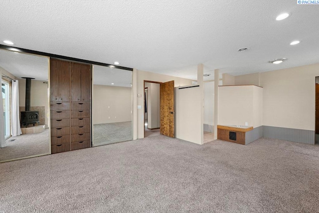 carpeted empty room featuring recessed lighting, a wood stove, and a textured ceiling