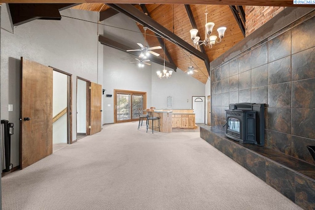 unfurnished living room with beam ceiling, wood ceiling, light carpet, a wood stove, and ceiling fan with notable chandelier