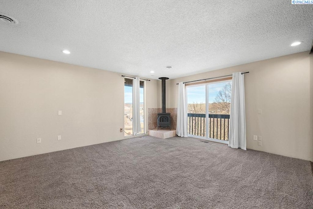 unfurnished living room featuring a wood stove, carpet, visible vents, and a textured ceiling