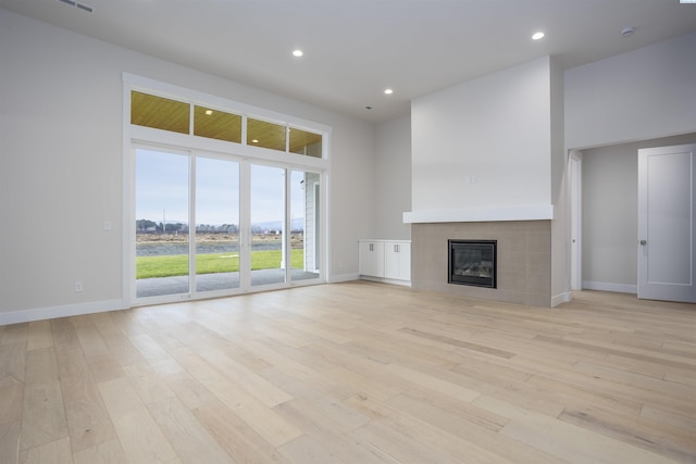 unfurnished living room with a towering ceiling, a fireplace, and light hardwood / wood-style flooring