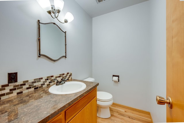 half bathroom with tasteful backsplash, visible vents, toilet, wood finished floors, and vanity