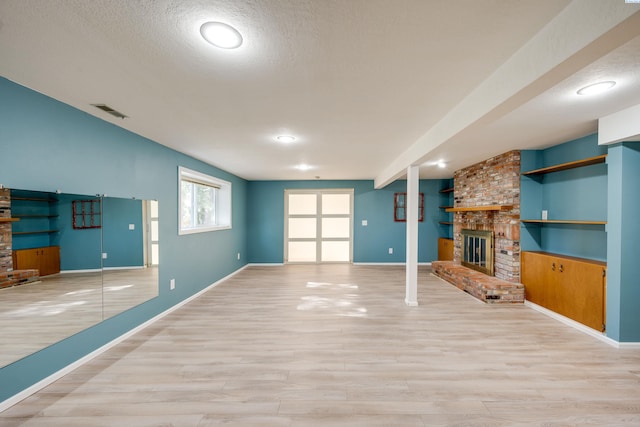 unfurnished living room with a brick fireplace, visible vents, light wood finished floors, and a textured ceiling