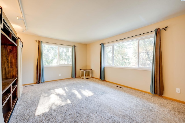 unfurnished living room featuring carpet floors, track lighting, visible vents, and baseboards